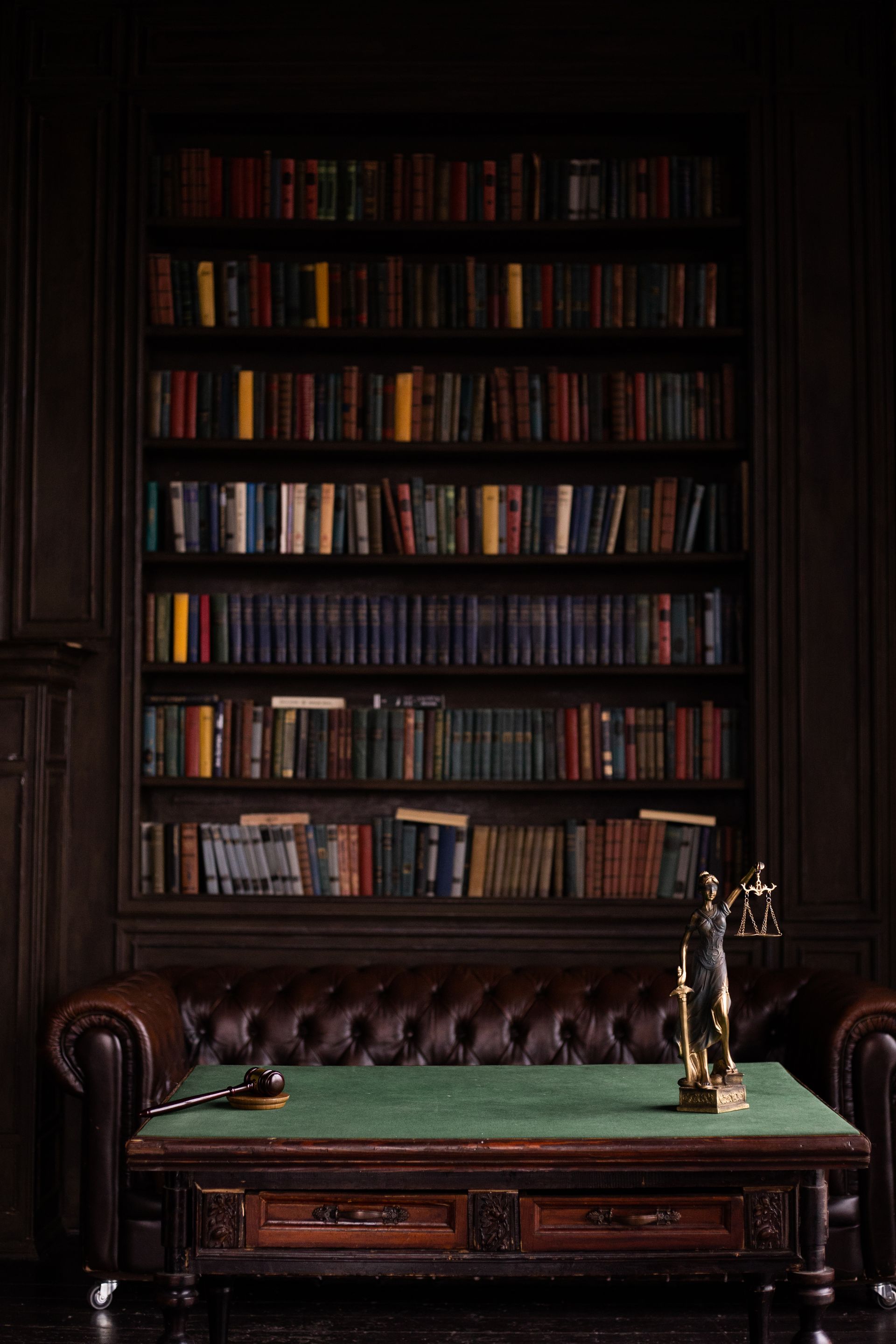 Classic law library study with leather chesterfield sofa, wood shelves, and Lady Justice